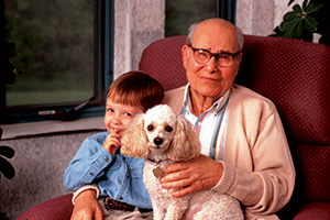 A Elderly gentleman sitting on the couch with his young grandson and a white dog