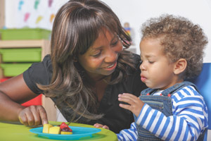 A caregiver looks on similing at a toddler