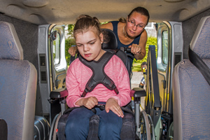 An adult helping a child in a wheel chair inside a car