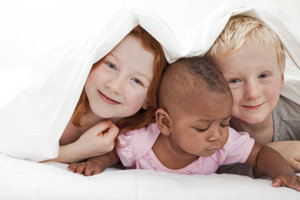 Three young kids looking at the camera happily from under a sheet