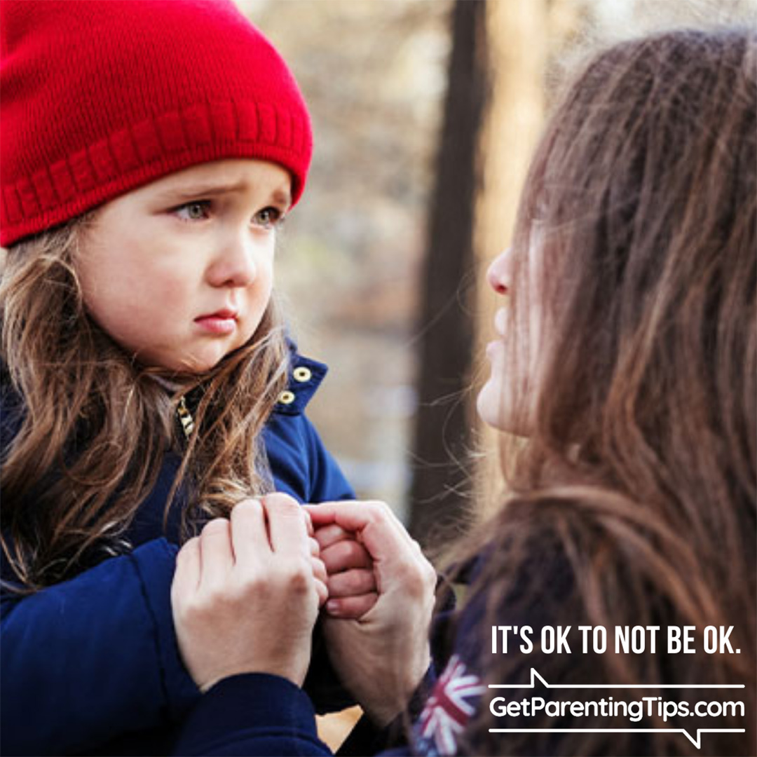 Mom holding her daughter's hands and talking with her. Text: It's OK to not be OK. GetParentingTips.com