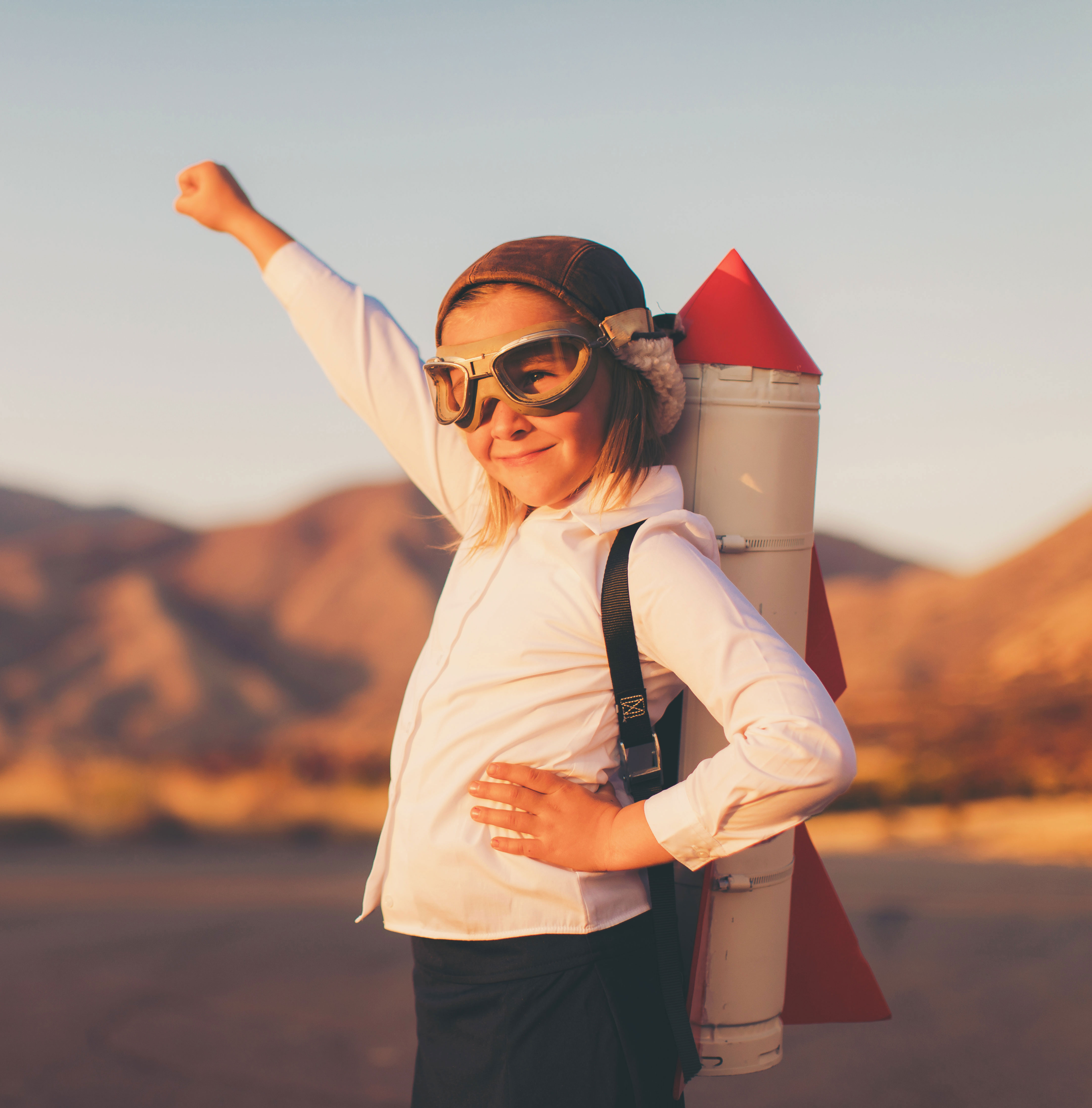 Kid wearing goggles and aviater hat with a rocket on her back