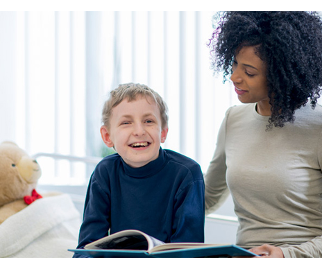 A lady sitting with a young boy with special needs on a hospital bed and reading